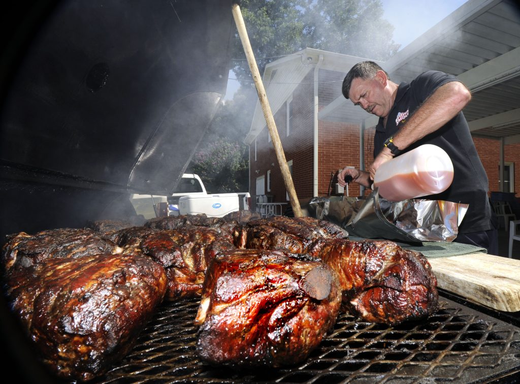 Jack Moore adding Blowin' Smoke sauce to the pork butts cooking in his barbeque pit. photo by Wayne Hinshaw, for the Salisbury Post